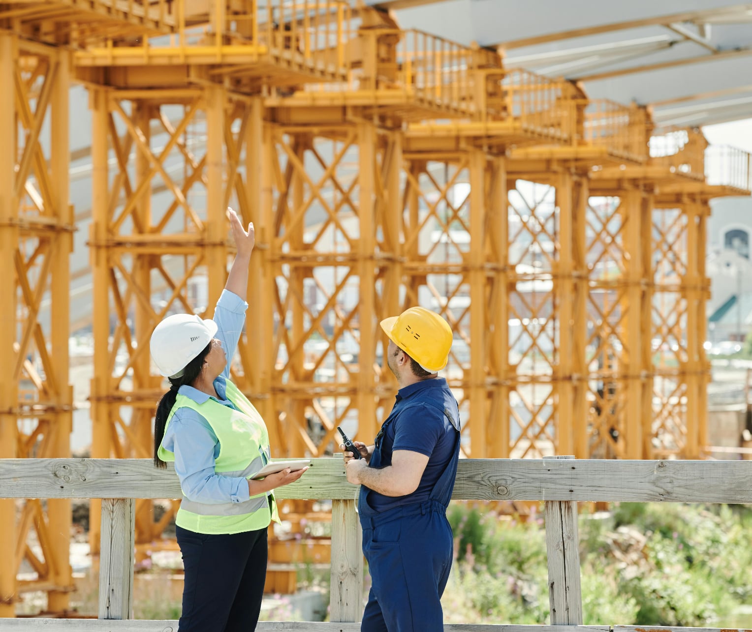 people in heard hats and a safety vest talking in front of yellow construction towers