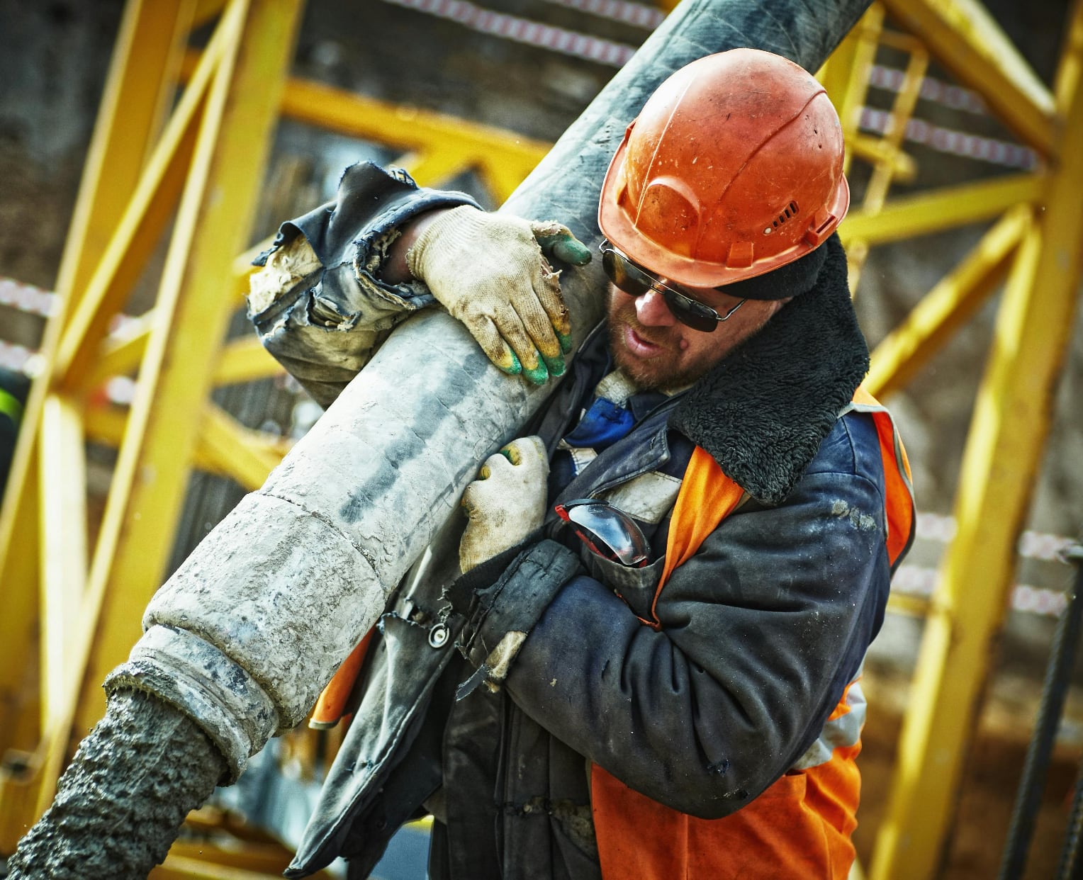 worker in hard hat and safety vest holding concrete hose with concrete flowing out