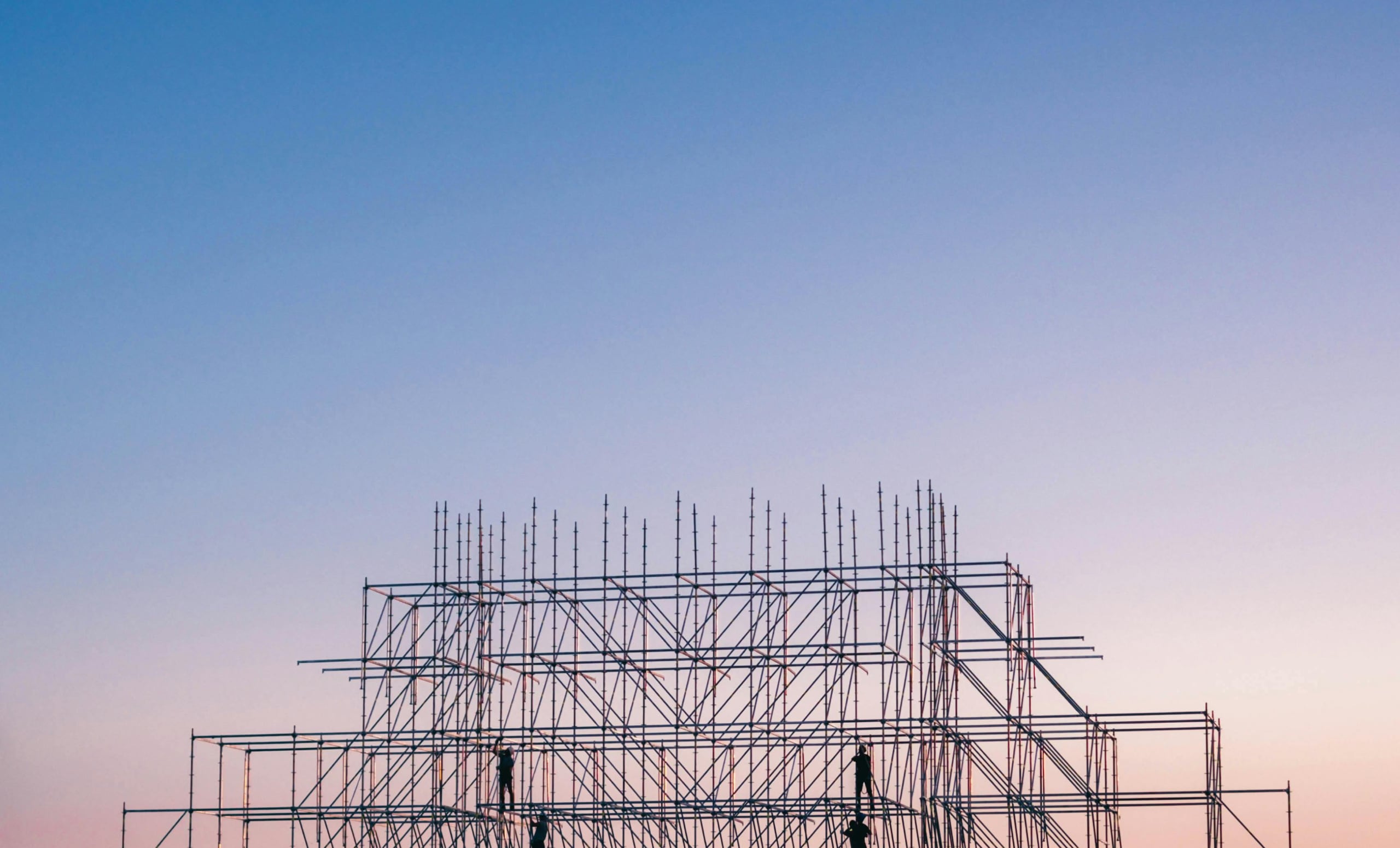 workers sillouetted on construction frame with pink sky in background