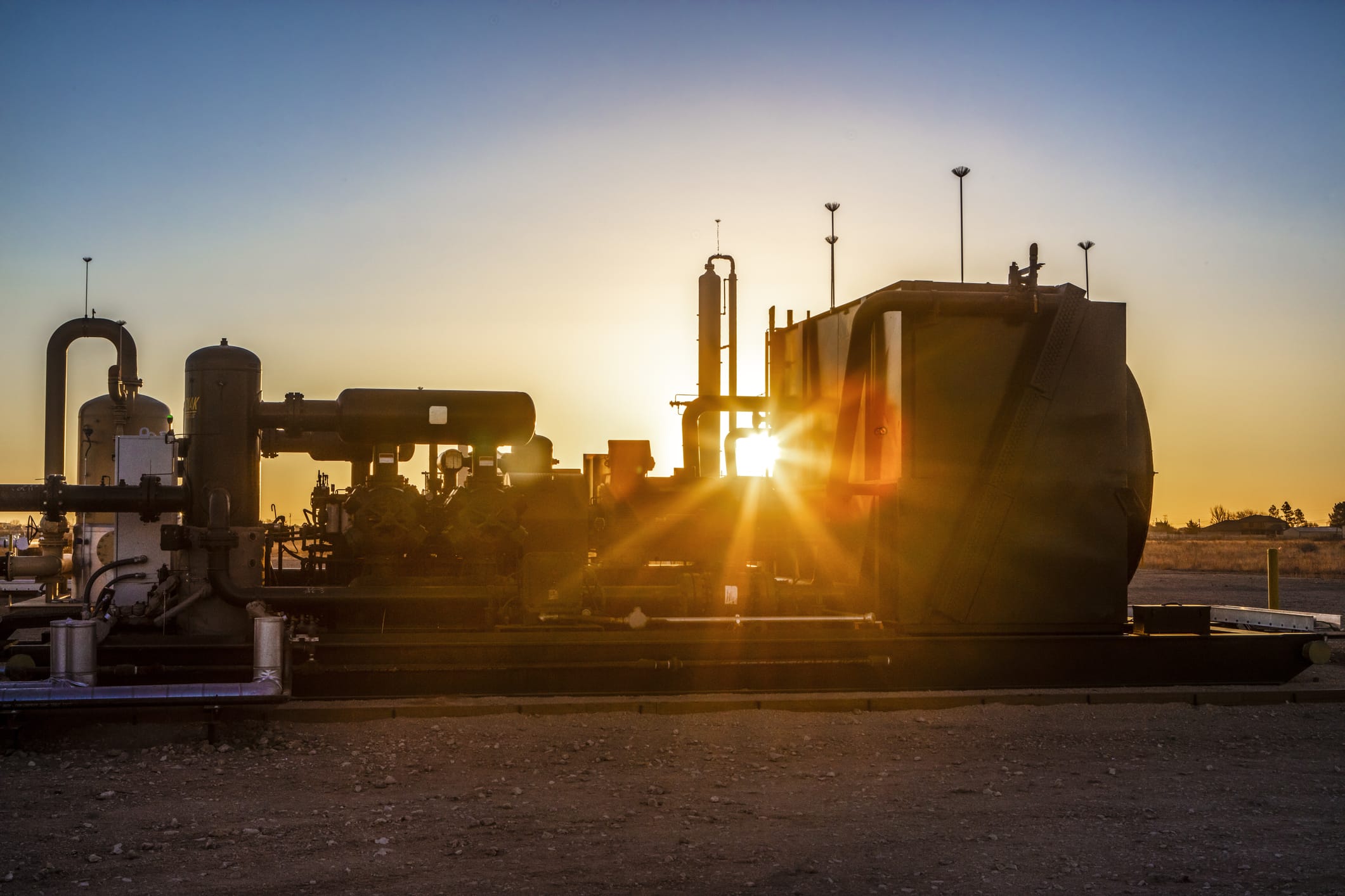 Sunset at a gas compressor field. Sun's rays peak through the machinery.